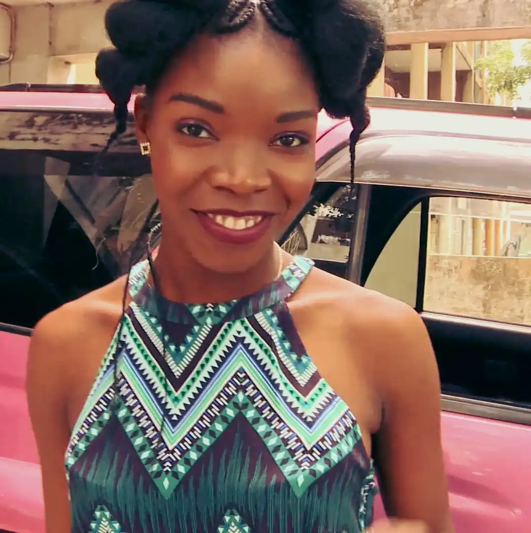 Smiling woman in a patterned teal dress stands in front of a pink vehicle.