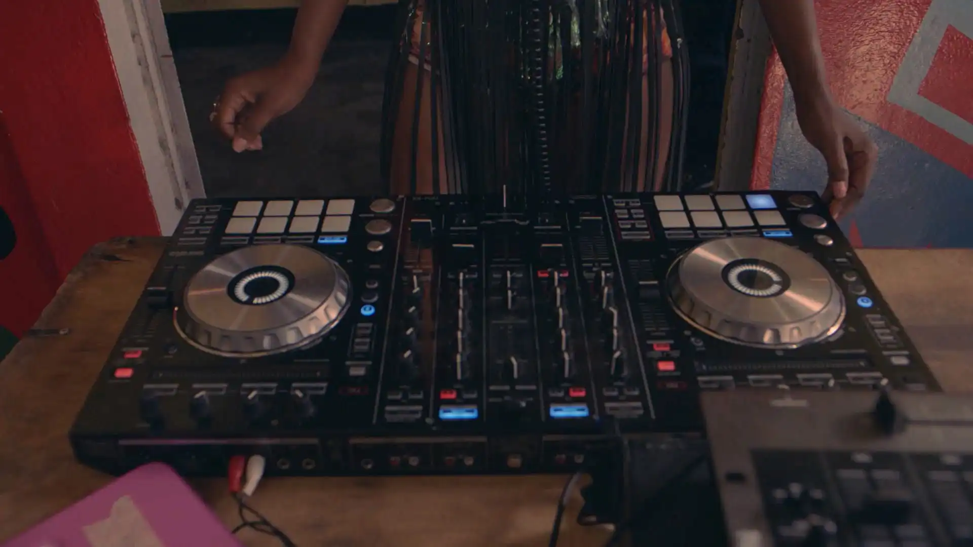 DJ mixing music on a dual turntable controller, with colorful lights and a vibrant atmosphere.