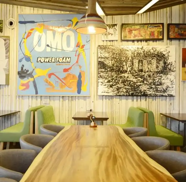 Casual dining area with colorful artwork, wooden tables, and green chairs, creating a vibrant and inviting atmosphere.