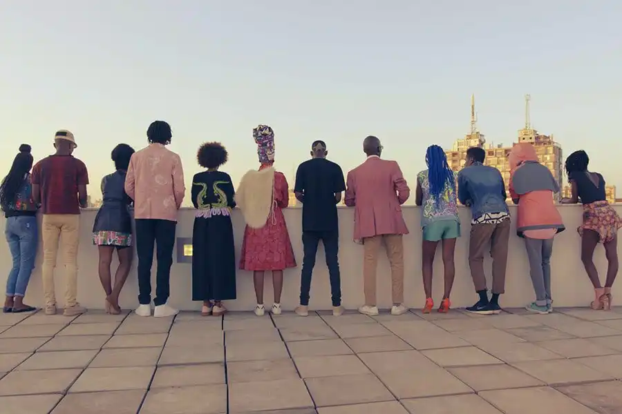 A diverse group of people stand on a rooftop, facing the city skyline.