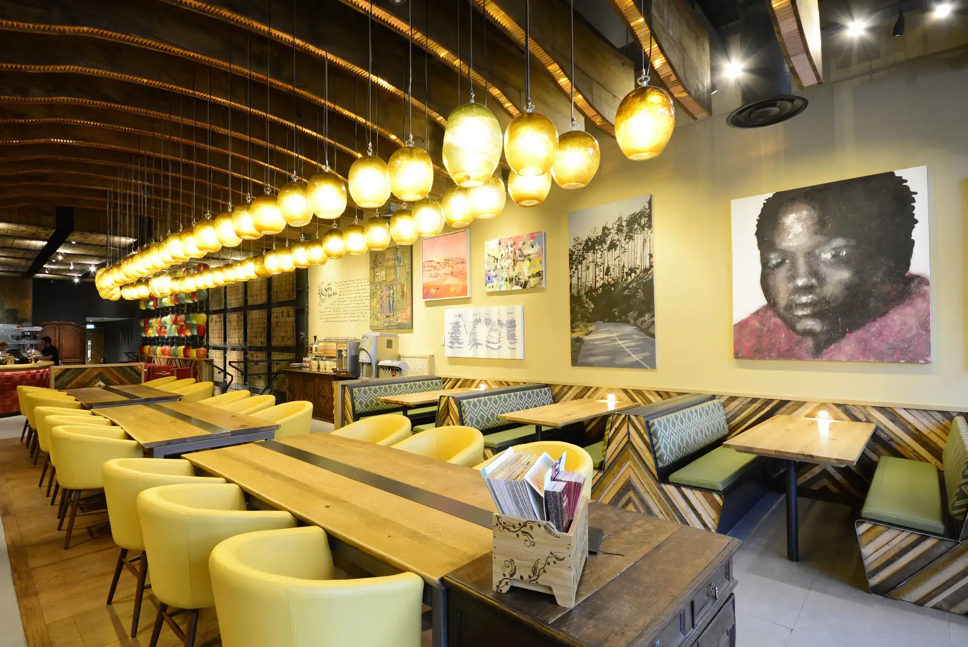 A vibrant Nando's restaurant interior with yellow chairs, wooden tables, hanging lights, and colorful artwork on the walls.