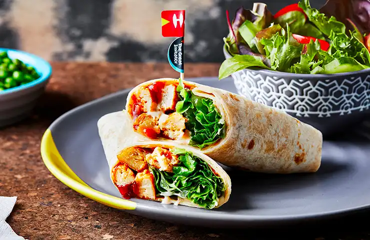 A Nando's wrap filled with flame-grilled PERi-PERi chicken, lettuce, and sauce, served with a side salad in a decorative bowl.